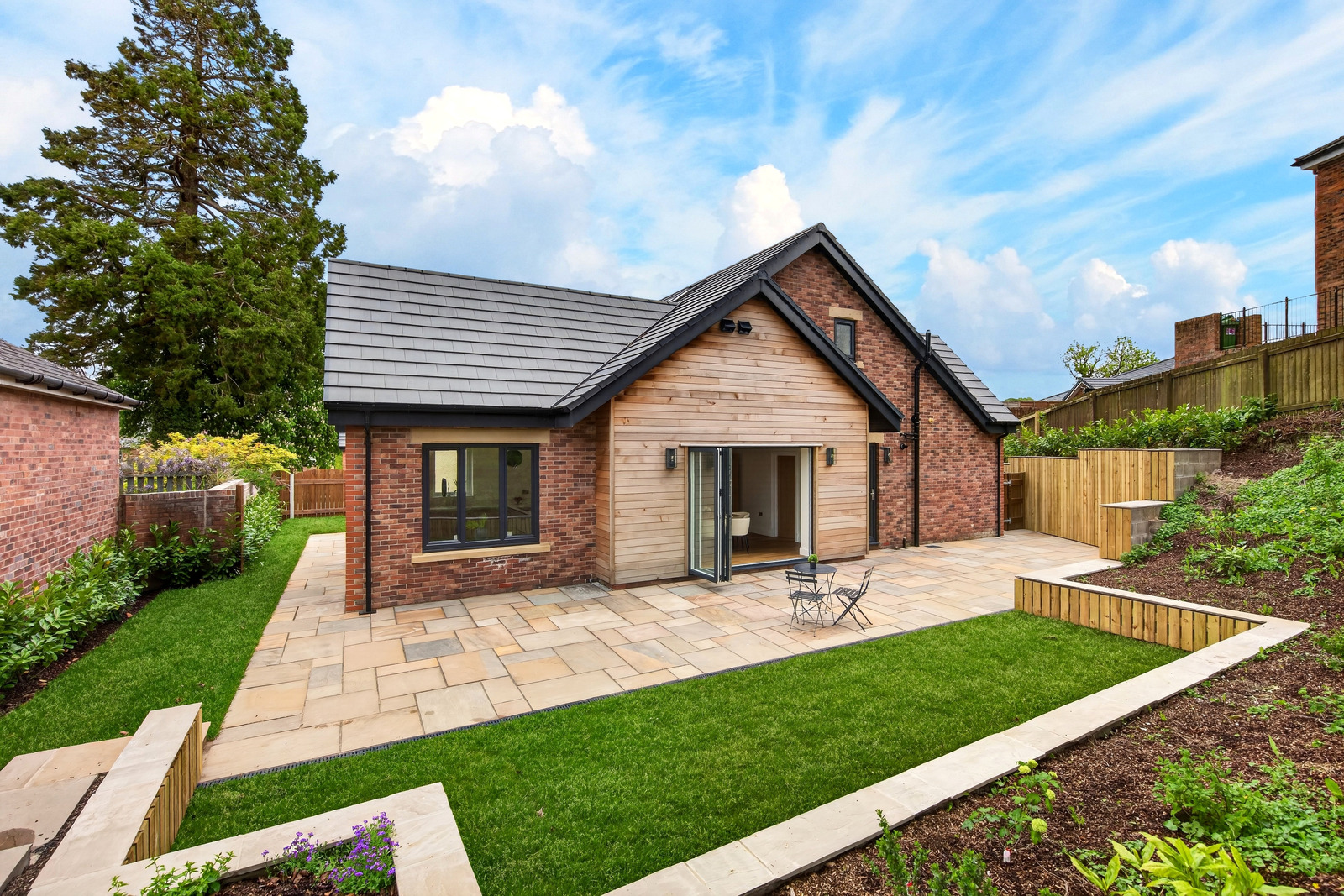 Rear garden view of an Orchard Place bungalow with sandstone patio, bi-fold doors and landscaped garden, Strawberry How Road, Cockermouth.
